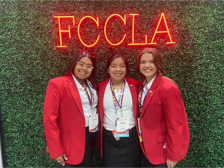 Cinthia Ríos, Sarai Velazquez, and Emma DeRise stand in front of a green background under red letters reading FCCLA